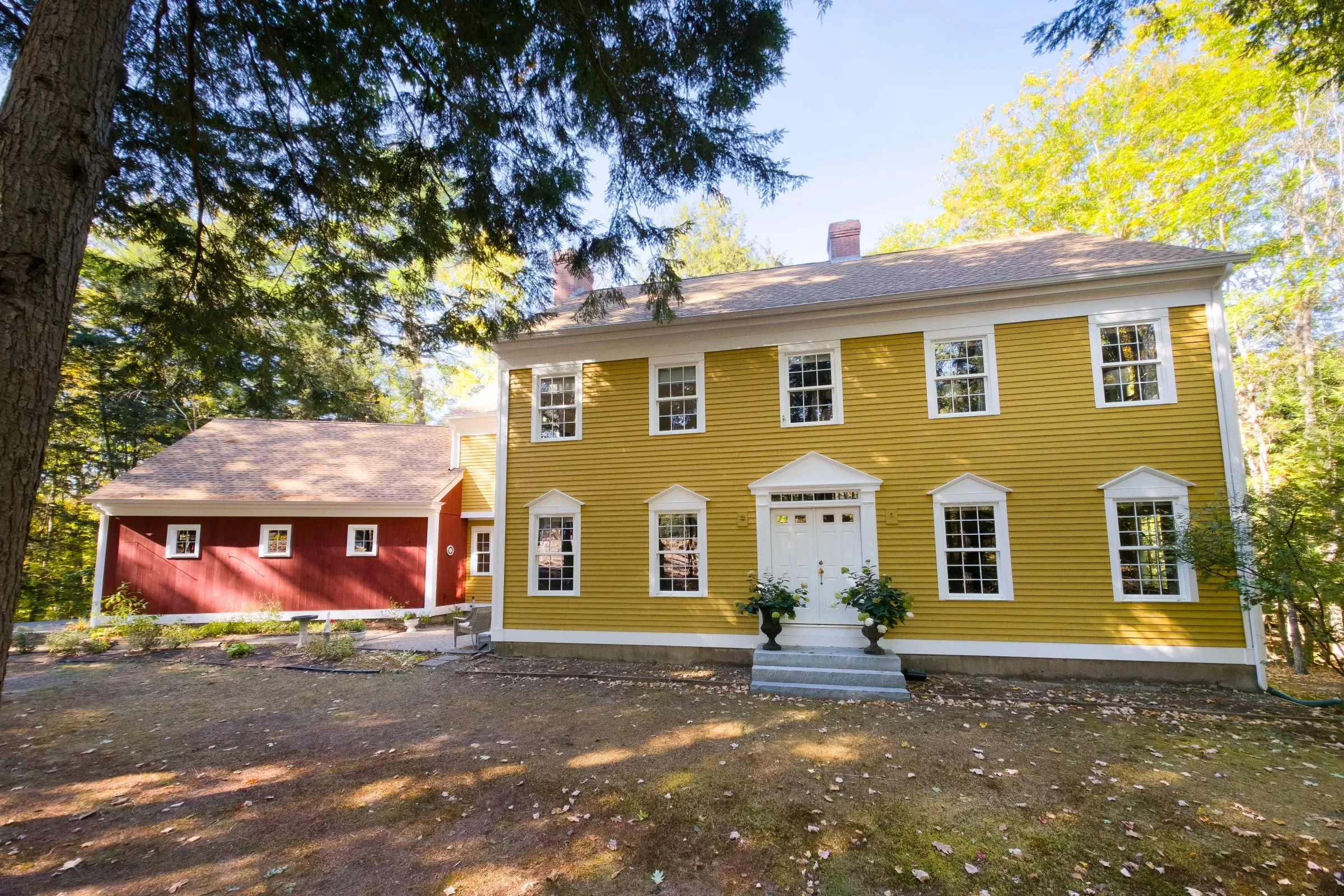 A yellow colonial home with white trim and a red barn, painted by Innovation Painting & Remodeling.