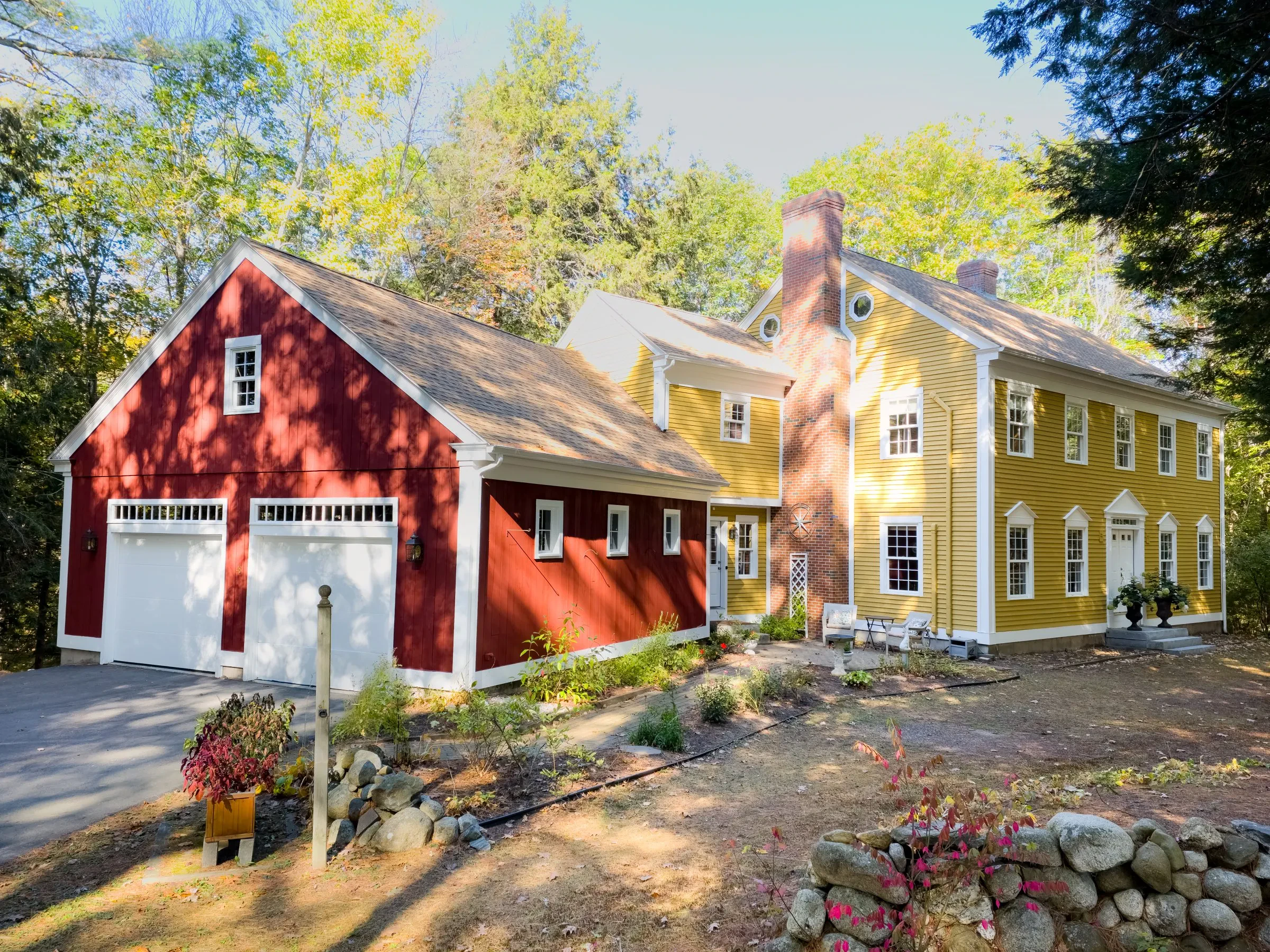 A yellow colonial home with a red barn garage, painted by Innovation Painting & Remodeling.